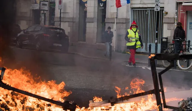 A demonstrator walks past burning debris during a protest called by the 'Yellow Vest' (gilets jaunes) anti-government movement as part of a nationwide multi-sector strike against the French government's pensions overhaul, on January 11, 2020 in Nantes, western France. - France's government on January 11, 2020, offered a possible compromise to unions waging a crippling, weeks-long transport strike against pension reform, offering to withdraw the most contested proposal that would in effect have raised the retirement age by two years. "To demonstrate my confidence in the social partners... I am willing to withdraw from the bill the short-term measure I had proposed" to set a so-called "pivot age" of 64 with effect from 2027, Prime Minister Edouard Philippe wrote in a letter to union leaders a day after they met seeking to end the labour action, now in its 38th day. (Photo by Loic VENANCE / AFP)