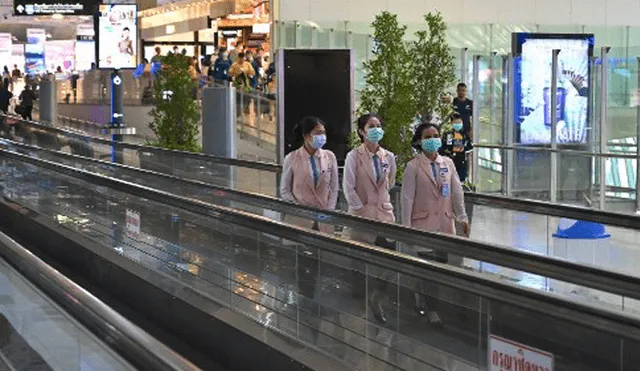 Empleados con máscaras protectoras viajan por una pasarela móvil en el aeropuerto de Suvarnabhumi en Bangkok. Foto: AFP.