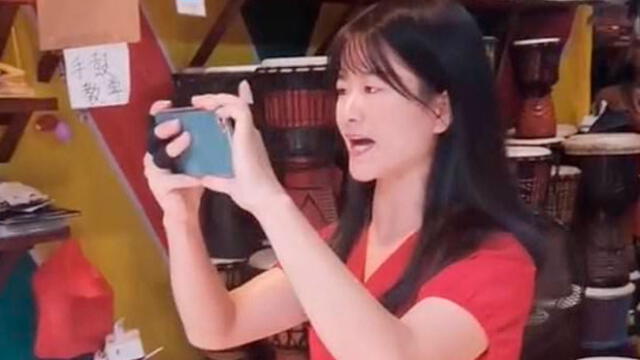 Mujer vestida de rojo graba con su teléfono a dos turistas que visitan su tienda. Foto: captura de pantalla.