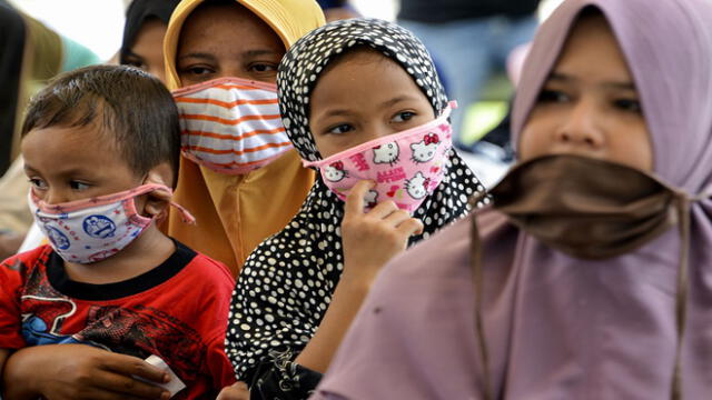 Women and children wearing face masks wait for food distribution amid the COVID-19 coronavirus pandemic in Blang Bintang, Aceh province on May 6, 2020. (Photo by CHAIDEER MAHYUDDIN / AFP)