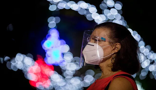 Una mujer usa mascarilla en una plaza decorada con luces navideñas en Caracas (Venezuela), donde hay disponibles bonos en el sistema Patria. Foto: EFE