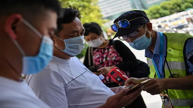 A worker wearing a face mask checks passengers body temperatures and a health code on their phones before they take a taxi after arriving at Hankou railway station in Wuhan, China's central Hubei province on May 12, 2020. - China reported no new domestic coronavirus infections on May 12, after two consecutive days of double-digit increases, including a new cluster over the weekend in Wuhan, which fuelled fears of a second wave of infections. (Photo by Hector RETAMAL / AFP)