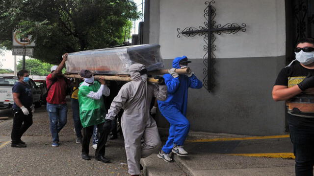 Relatives of a person who died from the new coronavirus -some in protective suits- carry the wrapped coffin inside a cemetery in the north of Guayaquil, Ecuador on April 17, 2020. (Photo by JOSE SANCHEZ LINDAO / AFP)
