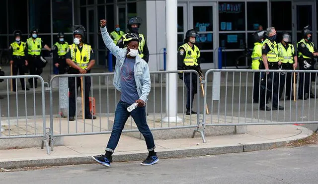 Un protestante pasa al frente de un cordón de policías puesto en la localidad de Boston, en otra manifestación tras la muerte de George Floyd. Foto: EFE