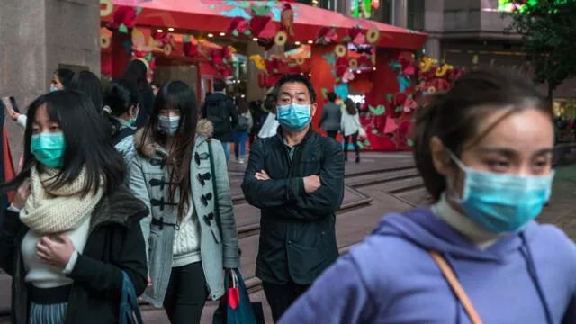 Las personas con máscaras se paran en una calle de un distrito comercial de Hong Kong el 26 de enero de 2020, como medida preventiva tras un brote de coronavirus que comenzó en la ciudad china de Wuhan.