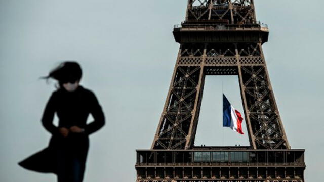Una mujer con una mascarilla camina mientras una bandera nacional francesa ondea en la Torre Eiffel/Foto: Phillipe López/AFP.