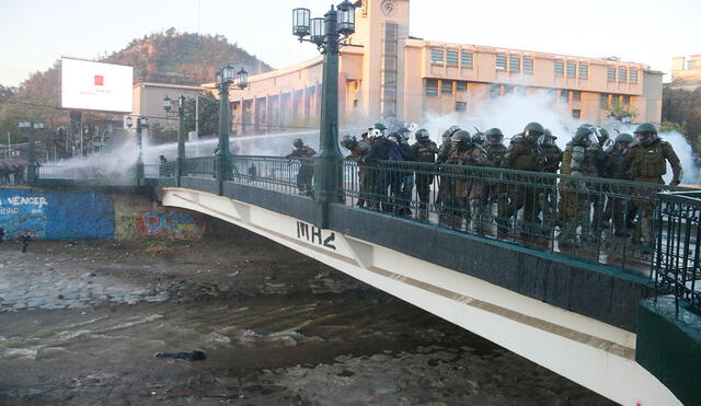 Miembros de carabineros observan a un manifestante que se encuentra inconsciente luego de caer en el río Mapocho. Foto: EFE