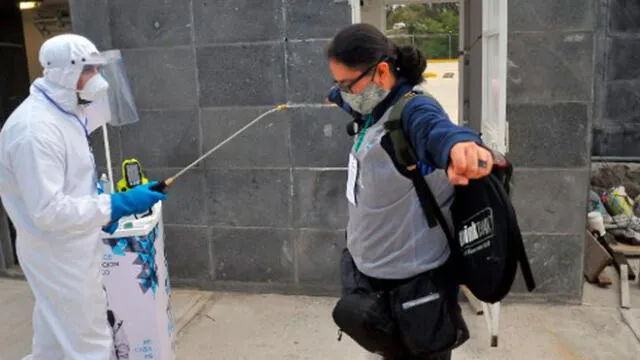 Un guardia de seguridad con equipo de protección personal rocía desinfectante sobre un fotógrafo en una puerta del estadio Cuauhtémoc en México. Foto: AFP.