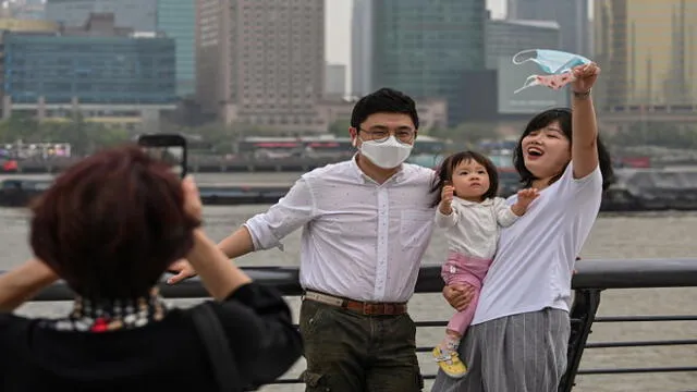People wearing face masks pose for a photo while visiting the promenade on the Bund along the Huangpu River during a holiday on May Day, or International Workers' Day, in Shanghai on May 1, 2020. - With optimism and a heavy dose of caution, millions of Chinese hit the road or visited newly re-opened tourist sites on May 1 for an extended national holiday in a post-coronavirus confidence test. (Photo by Hector RETAMAL / AFP)