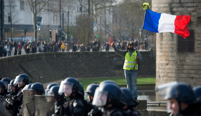A demonstrator stands behind the police line as he hold the French flag during a protest called by the 'Yellow Vest' (gilets jaunes) anti-government movement as part of a nationwide multi-sector strike against the French government's pensions overhaul, on January 11, 2020 in Nantes, western France. - France's government on January 11, 2020, offered a possible compromise to unions waging a crippling, weeks-long transport strike against pension reform, offering to withdraw the most contested proposal that would in effect have raised the retirement age by two years. "To demonstrate my confidence in the social partners... I am willing to withdraw from the bill the short-term measure I had proposed" to set a so-called "pivot age" of 64 with effect from 2027, Prime Minister Edouard Philippe wrote in a letter to union leaders a day after they met seeking to end the labour action, now in its 38th day. (Photo by Loic VENANCE / AFP)
