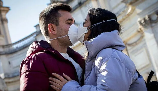 Dos personas se besan con mascarillas por precaución ante la COVID-19. Foto: AFP