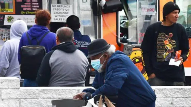 Un anciano con una mascarilla pasa junto a unas personas que esperaban en la fila de un Food Truck en Los Ángeles. Foto: AFP.