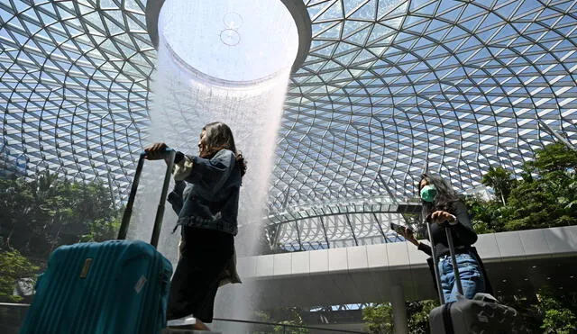 A traveller (R), wearing a protective facemask amid fears about the spread of the COVID-19 novel coronavirus, walks past the Rain Vortex display at Jewel Changi Airport in Singapore on February 27, 2020. (Photo by Roslan RAHMAN / AFP)