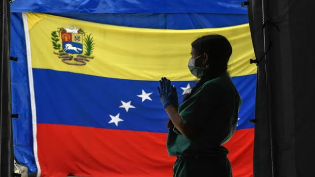 A staff member of Doctors Without Borders prepares herself waits for patients to be tested for COVId-19 in front of a Venezuelan flag at the Perez de Leon Hospital os the Petare neighbourhood, in eastern Caracas on June 23, 2020, amid the new coronavirus pandemic. - In Petare, the largest slum in Venezuela, more than 100 professionals of Doctors Without Borders face the COVID-19 pandemic getting around the crisis in the country's public healthcare sector. (Photo by Federico PARRA / AFP)
