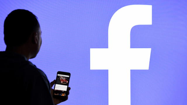 15 March 2019, Schleswig-Holstein, Aukrug-Homfeld: ILLUSTRATION - A man with a smartphone stands in front of a monitor with the Facebook logo. (Credit Image: © Carsten Rehder/DPA via ZUMA Press)