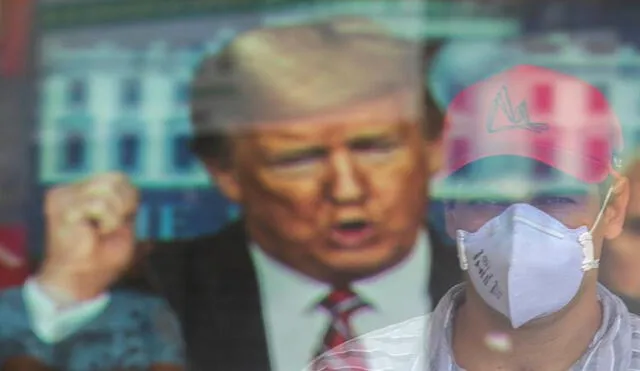 Un hombre con tapabocas aparece reflejado mientras observa un anuncio con el presidente estadounidense, Donald Trump, este lunes, en Brasilia (Brasil). Foto: EFE