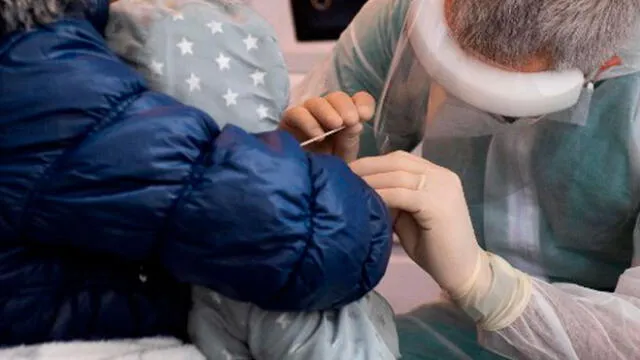 Una persona sostiene a su niño pequeño mientras se le hacen una prueba rápida de hisopado de antígeno para la COVID-19. Foto: AFP
