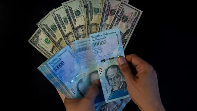 A man counts Venezuelan bolivar banknotes next to US dollar bills in Caracas on August 2, 2018. - Venezuela's government on Thursday loosened the tight currency controls it first put in place 15 years ago, with the pro-government Constituent Assembly announcing the passage of a decree authorizing money exchange operations. (Photo by Federico PARRA / AFP)