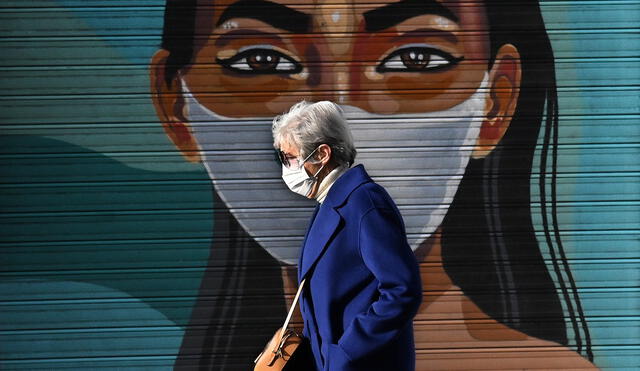 Una mujer con mascarilla para protegerse del coronavirus pasa junto al mural de una joven con mascarilla, en Madrid. Foto: AFP.