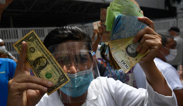 A health worker wearing a face mask and shield holds a one dollar bill in one hand and its equivalent in Bolivar bills -his salary- in the other, during a protest for the lack of medicines, medical supplies and poor conditions in hospitals, in Caracas on October 29, 2020, amid the new coronavirus pandemic. (Photo by Federico PARRA / AFP)