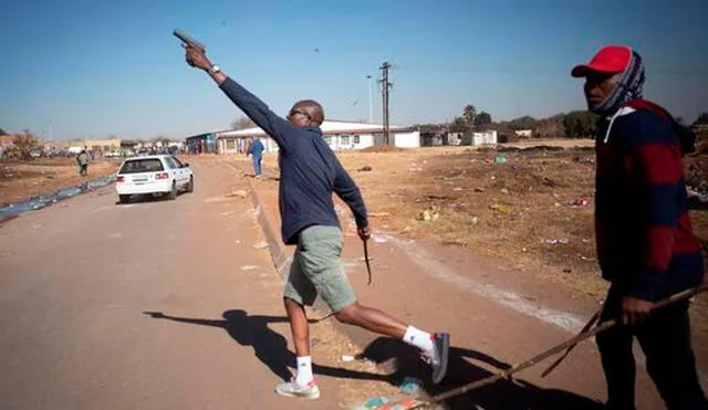 Un taxista dispara al aire con su pistola 9mm para ahuyentas a los saqueadores en un área comercial de Johannesburgo. Foto: EFE