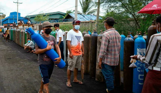 Un hombre carga un tanque de oxígeno mientras otros hacen fila para cargar los suyos en una planta de Mandalay, Birmania, el 13 de julio de 2021. Foto: AFP