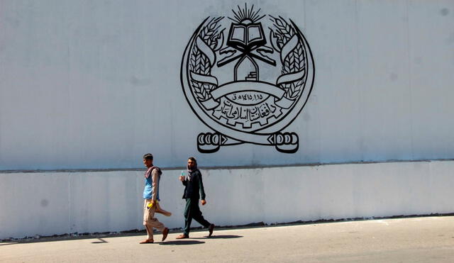 Afganos transitan al frente de la antigua embajada estadounidense, en cuya pared está el sello del gobierno talibán: Emirato Islámico de Afganistán. Foto: EFE