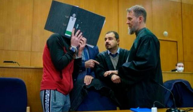 Taha al Juamilly se cubre el rostro mientras habla con sus abogados antes de ser sentenciado, el 30 de noviembre de 2021 en un tribunal alemán. Foto: AFP