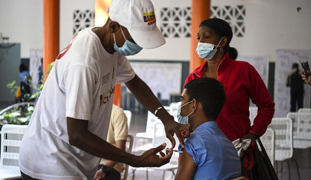 Un joven acompañado por su madre está siendo inoculado con Vero Cell, una vacuna contra la COVID-19. Foto: AFP