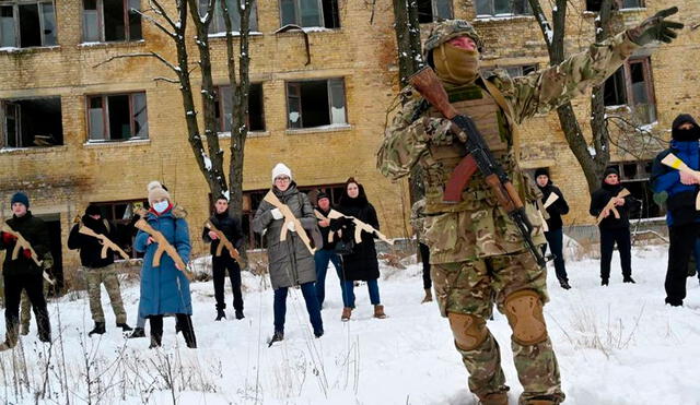 Un instructor militar enseña a civiles que sostienen réplicas de madera de rifles Kalashnikov, durante una sesión de entrenamiento en una fábrica abandonada en la capital de Ucrania. Foto: AFP