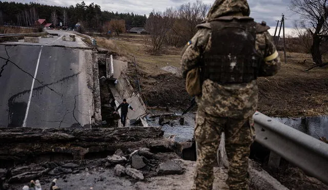 Un militar ucraniano mira a un civil cruzando un puente volado en una aldea, al este de la ciudad de Brovary, el 6 de marzo de 2022. Foto: AFP