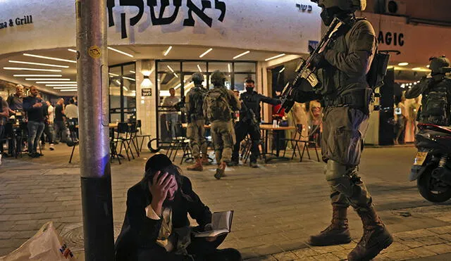 Un hombre judío reacciona mientras sostiene un volumen del Libro de los Salmos mientras las fuerzas de seguridad se reúnen detrás de la escena del ataque. Foto: AFP