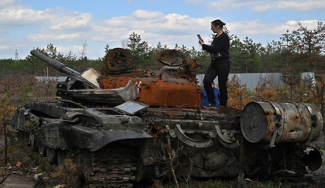 Una mujer toma una fotografía mientras se encuentra en un tanque ruso destruido en la aldea de Dmytrivka, región de Kiev. Foto: AFP