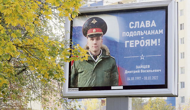 Propaganda militar. Ciudadanos rusos conversan bajo el cartel del soldado Dmitry Zaitsev, muerto en la invasión a Ucrania. Foto: EFE