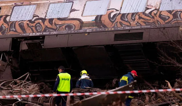  Un policía y 2 hombres inspeccionan el terreno bajo uno de los vagones descarrilados, en el terrible accidente de tren que se ha producido en el centro de Grecia. Foto: EFE    