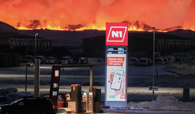 Varias personas recargan sus vehículos en una gasolinera mientras la lava y el humo salen de una fisura durante una erupción volcánica cerca de Grindavik. Foto: AFP   