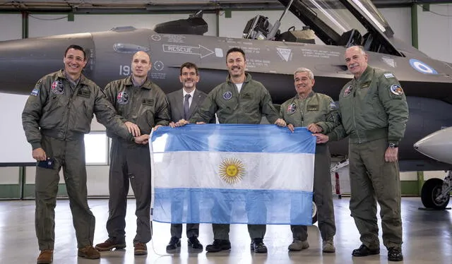 Los miembros de la delegación argentina, incluido el ministro de Defensa, Luis Alfonso Petri, sostienen su bandera nacional mientras posan frente a un caza F-16 que compró Argentina a Dinamarca. Foto: AFP   