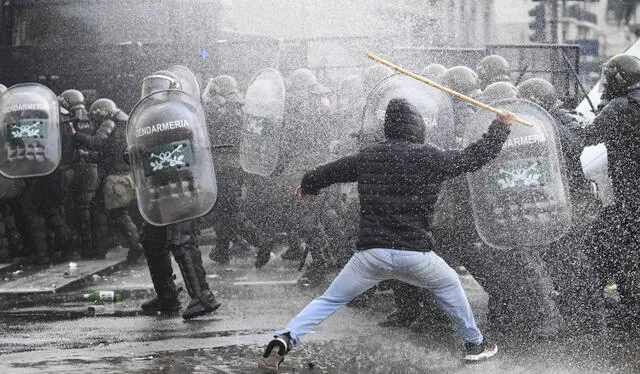 Un manifestante choca con la policía antidisturbios mientras es rociado por un cañón de agua de la policía frente al Congreso Nacional. Foto: AFP   