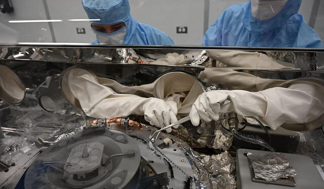 Los procesadores de astromateriales Mari Montoya, izquierda, y Curtis Calva, derecha, utilizan herramientas para recolectar partículas de asteroides de la base del recipiente científico OSIRIS-REx. Foto: NASA   