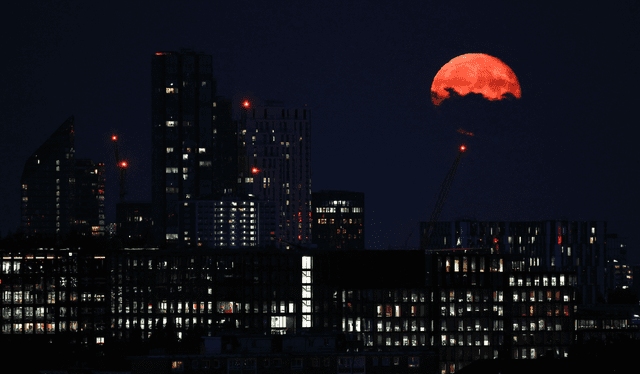 Luna con tonalidad rojiza fue fotografiada tras los edificios residenciales y de oficinas en el distrito comercial de Canary Wharf. Foto: Henry Nicholls/AFP    