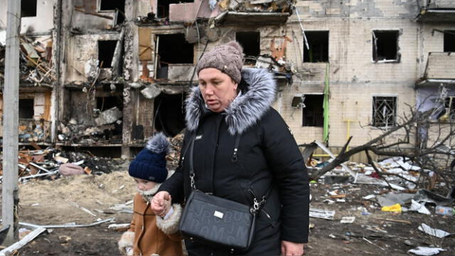  Una mujer con un niño camina frente a un edificio residencial dañado en la calle Koshytsa, un suburbio de la capital ucraniana, Kiev, donde supuestamente cayó un proyectil militar. | Fuente: AFP    