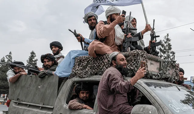 Talibanes sostienen armas mientras viajan en un convoy para celebrar el día de su victoria cerca del aeropuerto de Kabul el 15 de agosto de 2022.