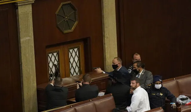 Oficiales de policía del Capitolio de los Estados Unidos apuntan con sus armas a una puerta que fue vandalizada en la Cámara de la Cámara durante una sesión conjunta del Congreso