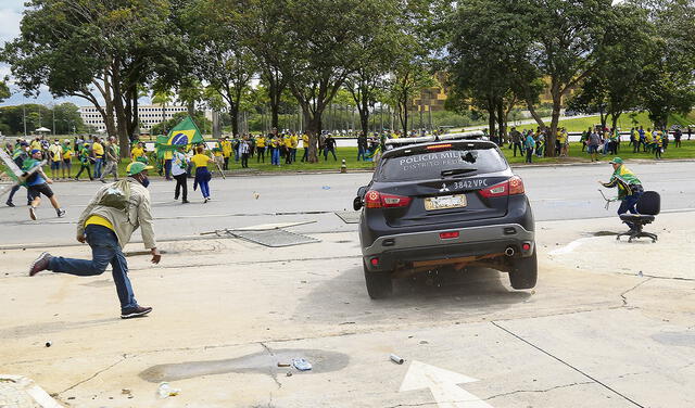 Vándalos. Bolsonaristas lanzan piedras a un patrullero de la policía federal luego del desalojo.Foto: EFE