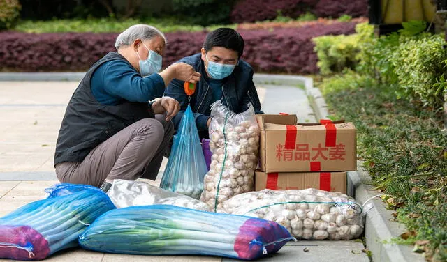 Dos residentes dan ajos y cebollas verdes en un complejo durante el confinamiento por COVID-19, en el distrito de Pudong (Shanghái). Foto: AFP