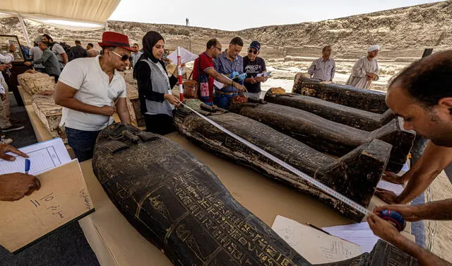 Arqueólogos miden la estatura de los sarcófagos durante el evento de exposición. Foto: AFP / Khaled Desouki