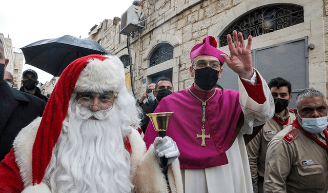 El arzobispo Pierbattista Pizzaballa saluda a la gente mientras camina al lado de un hombre disfrazado de Santa Claus en la ciudad de Belén. Foto: AFP