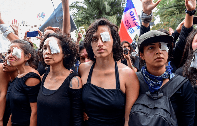 Mujeres vestidas de negro y con parches en los ojos representan a los manifestantes heridos con perdigones disparados por la policía antidisturbios. Foto: AFP   