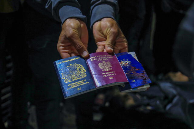 Un hombre muestra pasaportes británicos, polacos y australianos junto a los cadáveres de trabajadores de World Central Kitchen. Foto: AFP   