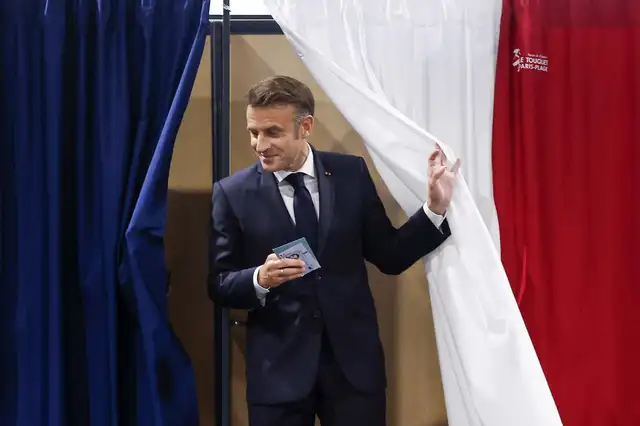 El presidente de Francia, Emmanuel Macron, sale de una cabina electoral, adornada con cortinas que muestran los colores de la bandera de Francia. Foto: AFP   